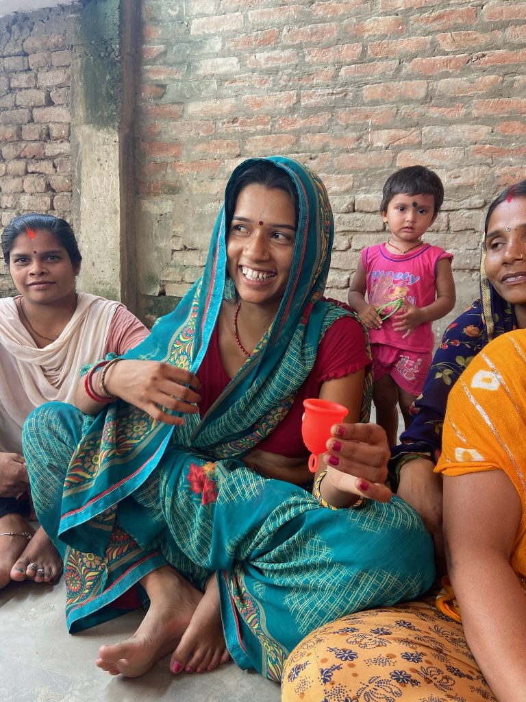 Women sat smiling holding a menstrual cup